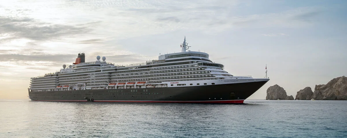 Cunard Queen Elizabeth anchored off Cabo San Lucas with dramatic coastal rock formations at sunrise